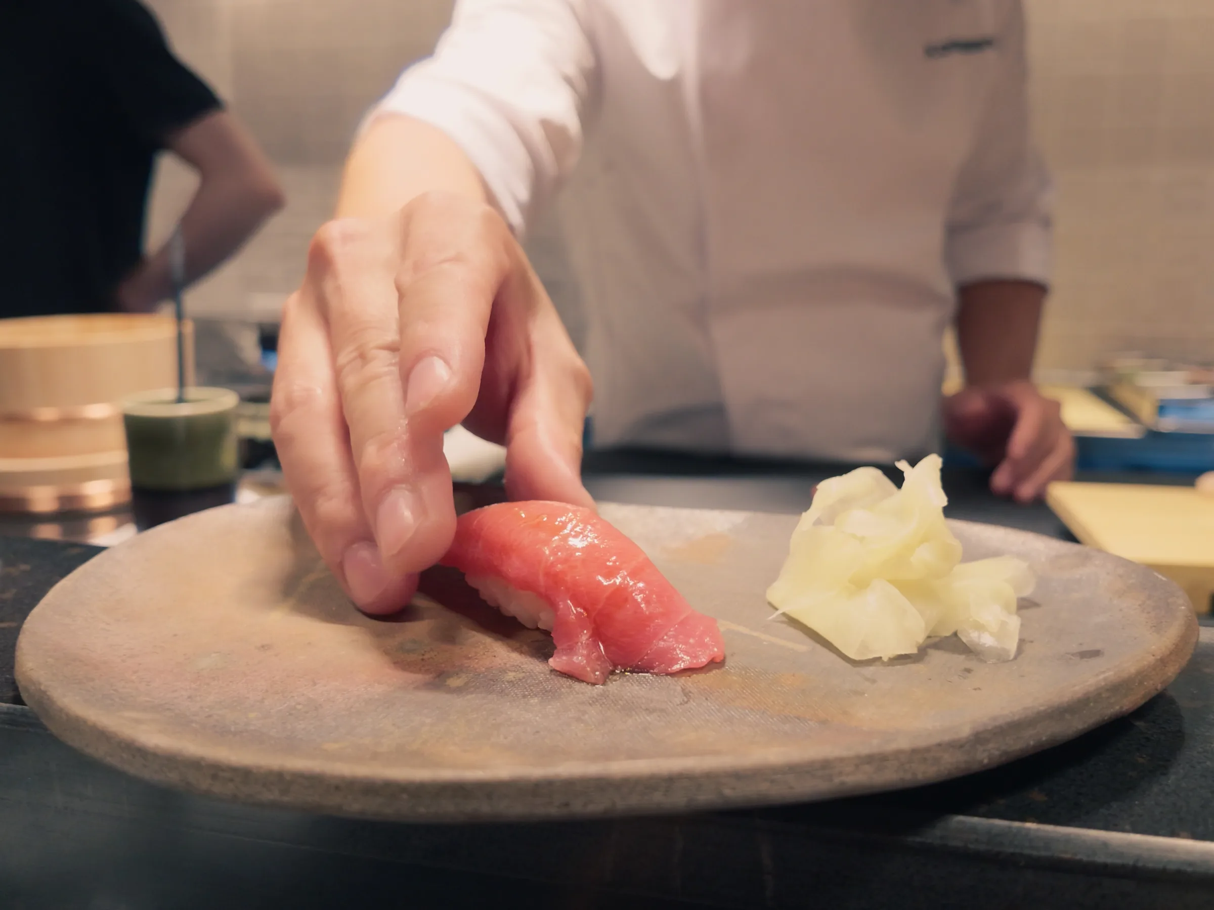Chef placing a piece of tuna nigiri on a plate at the counter
